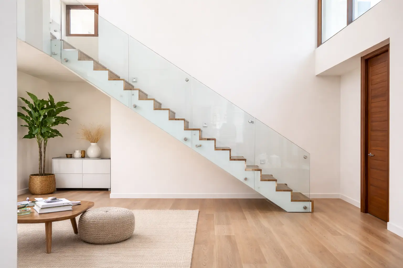 Parapetto in vetro per interni su scala moderna con pannelli trasparenti fissati lateralmente, gradini in legno chiaro e ambiente minimal luminoso.